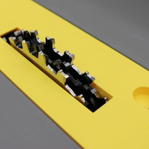 May include: Close-up of a table saw blade. The blade is silver and has sharp teeth. It is set in a yellow and gray table. The saw is designed for cutting wood and other materials.