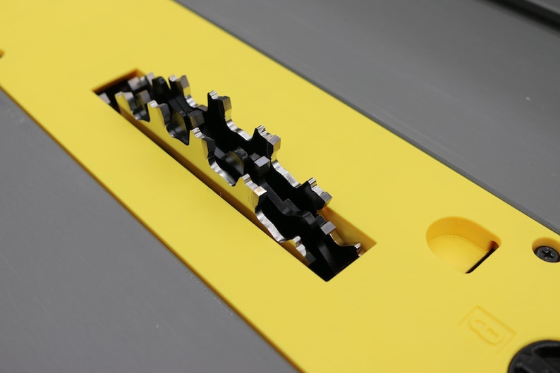May include: Close-up of a table saw blade. The blade is silver and has sharp teeth. It is set in a yellow and gray table. The saw is designed for cutting wood and other materials.