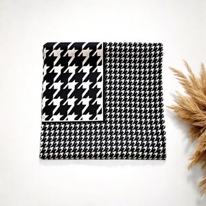 May include: Black and white patterned fabric with a houndstooth design. The fabric is folded in half and has a smooth texture.