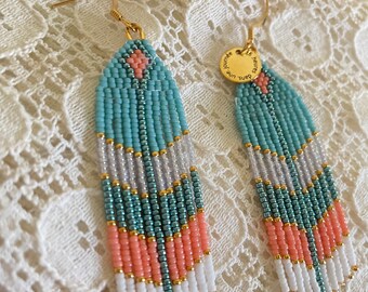 May include: A pair of turquoise, white, and coral beaded earrings with gold accents. The earrings have a small gold charm with the text "C'est une super journée".