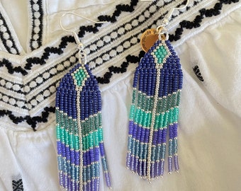 May include: A pair of long, beaded earrings with a blue, green, and silver color scheme. The earrings are made of small, round beads and have a tassel-like design. The earrings are hanging from silver hooks.