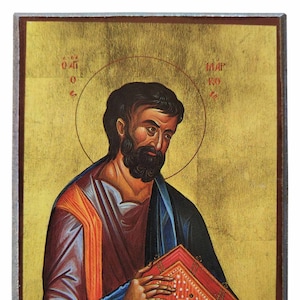 May include: Icon depicting a man with a beard, holding a red book. The man wears a blue and red robe, with a gold halo. The background is gold, with text in Greek.