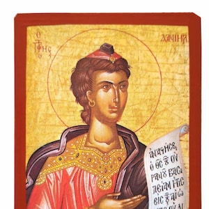 May include: A religious icon depicting a person holding a scroll with text in Greek. The icon is painted in a traditional style with gold and red accents. The text on the scroll reads "πάντα εις ο θεος ου παυς εασι λεϊμη ηις εις ξαις ηας ου αι αφορη σεται."
