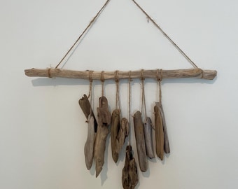 Può includere: Un'appendice da parete in legno di deriva con più pezzi di legno di deriva appesi a un unico ramo. Il legno di deriva è legato insieme con uno spago e pende da un triangolo di spago.