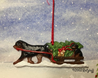 Rottweiler with puppy on sled. Bringing the Christmas tree home. Dog breed ornament by J Ratzlaff.