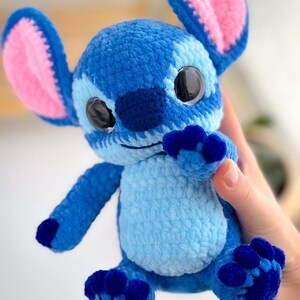 Puede incluir: Un peluche azul tejido a mano con grandes ojos negros, orejas grandes con interior rosa y detalles en azul oscuro. El peluche tiene una barriga azul claro y pies azul oscuro. El juguete es un personaje de una popular pel&iacute;cula de animaci&oacute;n.