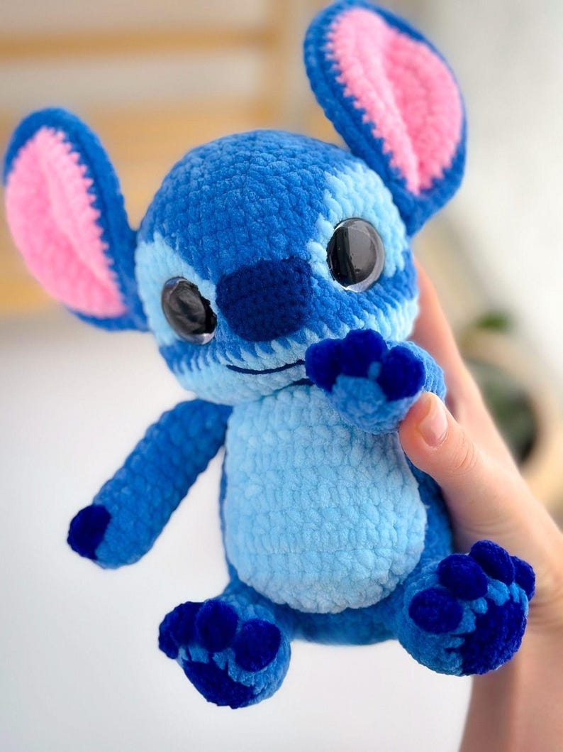 Puede incluir: Un peluche azul tejido a mano con grandes ojos negros, orejas grandes con interior rosa y detalles en azul oscuro. El peluche tiene una barriga azul claro y pies azul oscuro. El juguete es un personaje de una popular pel&iacute;cula de animaci&oacute;n.