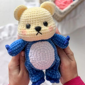 Peut inclure: Un ours en peluche crochet&eacute; &agrave; la main, de couleur cr&egrave;me et bleu. L'ours a une t&ecirc;te et des oreilles de couleur cr&egrave;me, avec un corps et des membres bleus. Il pr&eacute;sente un ventre blanc, des yeux noirs et un petit nez noir. L'ours est doux et moelleux.