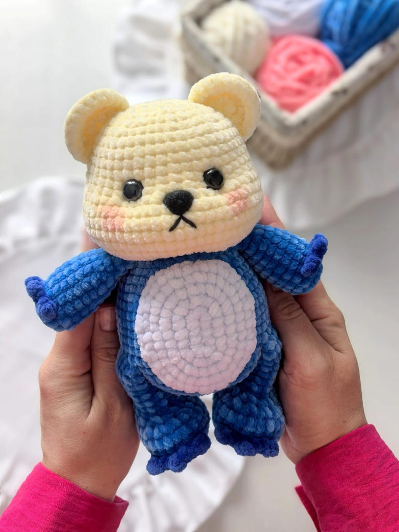 Peut inclure: Un ours en peluche crochet&eacute; &agrave; la main, de couleur cr&egrave;me et bleu. L'ours a une t&ecirc;te et des oreilles de couleur cr&egrave;me, avec un corps et des membres bleus. Il pr&eacute;sente un ventre blanc, des yeux noirs et un petit nez noir. L'ours est doux et moelleux.