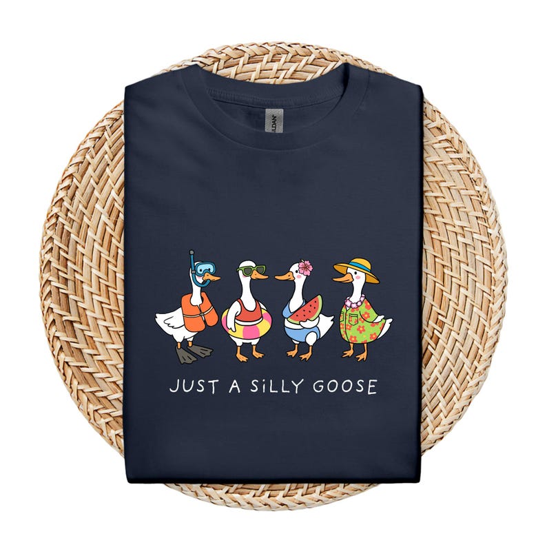 May include: Navy blue t-shirt featuring a whimsical illustration of four geese in summer attire. One goose wears a snorkel, another sunglasses, a third holds a watermelon slice, and the last wears a Hawaiian shirt and hat. The text "JUST A SILLY GOOSE" is printed below.