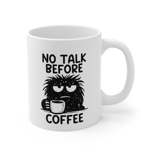 May include: White ceramic coffee mug with a black illustration of a grumpy monster holding a coffee cup. The mug has the text "NO TALK BEFORE COFFEE" in black, bold letters.