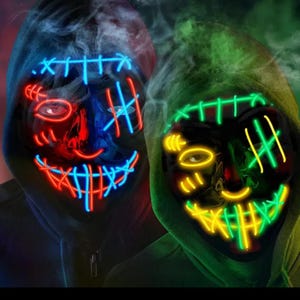 May include: Two black masks with glowing neon designs. One mask has red and blue accents, the other has green and yellow. Both masks have a stitched-mouth design and are worn with a hooded sweatshirt.