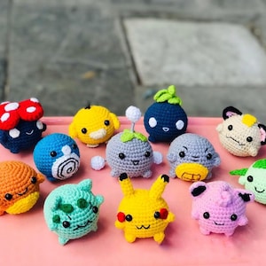 Pode incluir: Uma coleção de brinquedos de pelúcia de crochê coloridos em várias formas e cores. Os brinquedos incluem um cogumelo, uma bola azul com um desenho em espiral, uma criatura amarela com uma folha e um Pikachu amarelo. Os brinquedos são feitos à mão.
