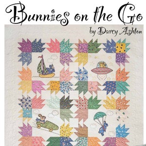 May include: A colorful quilt pattern featuring six bunnies in different vehicles, including a car, a plane, a boat, and a spaceship. The quilt is made up of 12-inch blocks and measures 60 inches by 84 inches. A smaller pillow with a bunny in a plane design is also included. The quilt is titled "Bunnies on the Go" by Darcy Ashton.