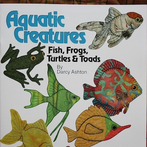 May include: A book titled "Aquatic Creatures: Fish, Frogs, Turtles & Toads" by Darcy Ashton. The cover features colorful illustrations of various aquatic animals, including fish, frogs, turtles, and toads.