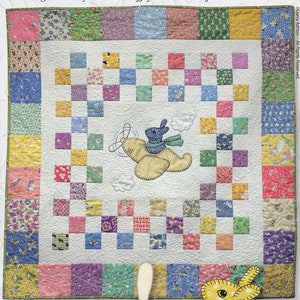Pode incluir: Um padrão de colcha com um coelho voando em um avião com o título "Bunny in the Sky". A colcha é feita de quadrados coloridos e tem 91 cm de tamanho. O padrão é de Darcy Ashton.
