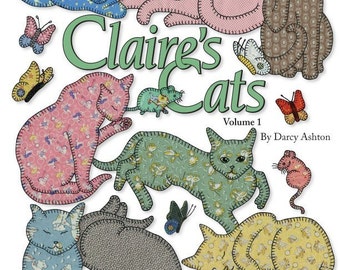 May include: A book cover with the title "Claire's Cats" in green text. The cover features a variety of colorful cats with floral patterns, butterflies, and a mouse. The book is volume 1 and is by Darcy Ashton.