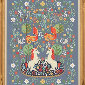 May include: A cross-stitch pattern featuring two white unicorns with gold horns and manes, facing each other in a whimsical forest scene. The background is a blue-grey color with a variety of colorful flowers, trees, and birds.