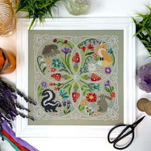 May include: Cross-stitch pattern featuring a circle of woodland animals and flowers. The animals include a fox, a skunk, a hedgehog, and a rabbit. The flowers are in shades of red, pink, yellow, blue, and green.