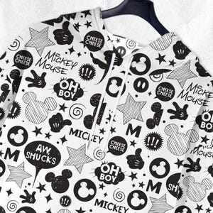Peut inclure: Sweat &agrave; capuche blanc avec un motif Mickey Mouse noir et blanc. Le motif comprend des silhouettes de Mickey Mouse, des &eacute;toiles, des bulles avec des phrases comme "Oh Boy" et "Aw Shucks", et les mots "Mickey Mouse".