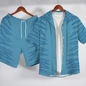 May include: A light blue matching set of shorts and a short-sleeved button-down shirt. The set features a pattern of darker blue curved lines. The shirt is open, revealing a white t-shirt underneath. The shorts have a white drawstring.