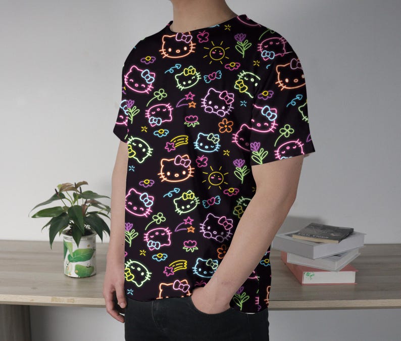 May include: Black t-shirt featuring a neon-style pattern of Hello Kitty characters, flowers, stars, and suns. The design includes pink, yellow, green, and blue outlines on a black background. The short-sleeved shirt is made of a soft material.