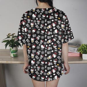 May include: Black short-sleeved shirt with an all-over print featuring Hello Kitty characters, bats, spiderwebs, and the text "Hello Kitty". The design includes white, red, and black elements.