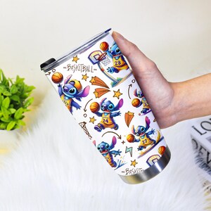 May include: A white stainless steel travel mug with a basketball theme, featuring the character Stitch. The design includes Stitch playing basketball, hoops, stars, and the word "Basketball". The mug has a black lid.