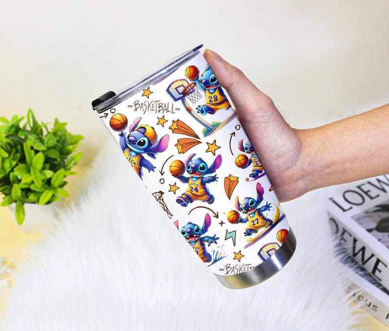 May include: A white stainless steel travel mug with a basketball theme, featuring the character Stitch. The design includes Stitch playing basketball, hoops, stars, and the word "Basketball". The mug has a black lid.