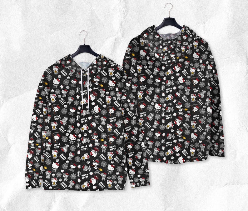 May include: Two black hoodies with a repeating pattern of Hello Kitty characters, snowflakes, and text. The hoodies are hanging on black hangers against a textured white background. The text reads "Hello Kitty".