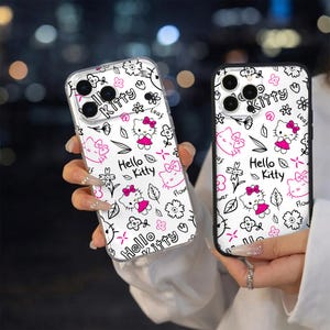 May include: Two phone cases with a white background and a repeating pattern of Hello Kitty, flowers, and leaves in black and pink. The cases have a clear, protective design.
