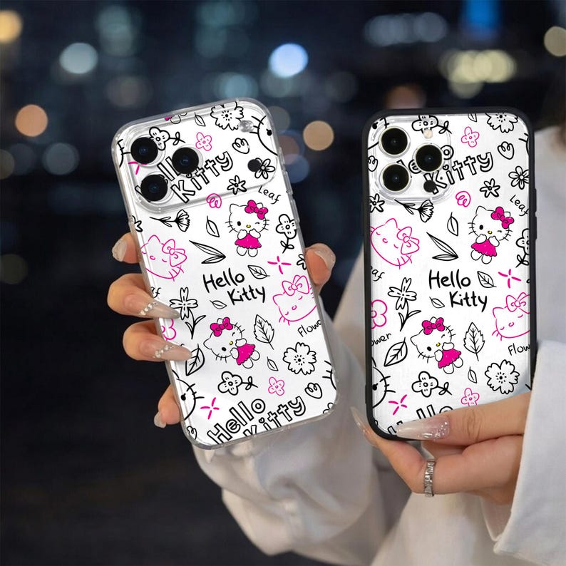 May include: Two phone cases with a white background and a repeating pattern of Hello Kitty, flowers, and leaves in black and pink. The cases have a clear, protective design.