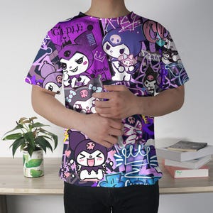 May include: A purple t-shirt with a cartoon character design, featuring illustrations and text. The short-sleeved shirt has a crew neck. The design incorporates shades of purple, white, and black.