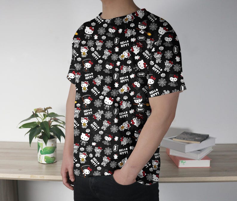 May include: Black t-shirt featuring a repeating pattern of Hello Kitty characters in various Halloween costumes, along with spiderwebs and the text "Hello Kitty". The design is in white, red, and black.