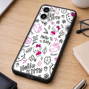 May include: A black phone case featuring a white background with a repeating pattern of Hello Kitty characters, flowers, and leaves in black and pink. The words "Hello Kitty" are also displayed in pink. The case is on a wooden surface.