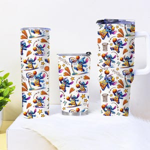 May include: Three white tumblers with a basketball-themed design featuring a blue cartoon character. The design includes basketballs, hoops, and stars. One tumbler is tall and cylindrical, another is shorter, and the third has a handle.