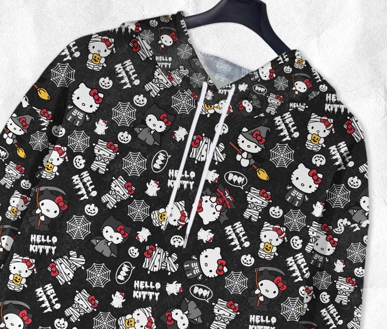 May include: Black hoodie featuring a repeating pattern of Hello Kitty characters in Halloween costumes, spiderwebs, pumpkins, and the text "Hello Kitty". The hoodie has a drawstring and is hanging on a black hanger.