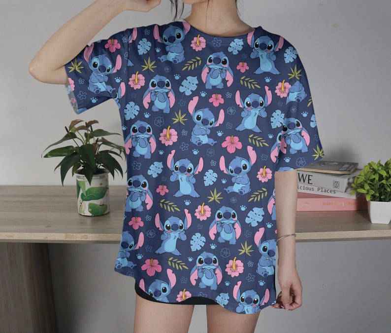 Pu&ograve; includere: Una maglietta blu navy con un motivo ripetuto del personaggio Stitch di Lilo & Stitch. Il design include Stitch, fiori rosa e foglie verdi.