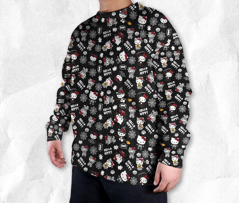 May include: Black long-sleeve shirt with an all-over print featuring Hello Kitty characters in Halloween costumes, pumpkins, spiderwebs, and the text "Hello Kitty". The design includes red, white, and black elements.