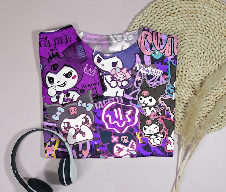 May include: A purple t-shirt with a vibrant graphic design featuring cartoon characters and graffiti-style text. The design incorporates characters in white, black, and purple, with the word "RAFFITI" visible. White and black headphones are in the foreground.