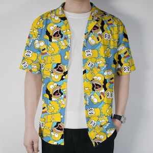 May include: Yellow button-down shirt with a repeating cartoon character pattern on a blue background. The shirt features short sleeves and a classic collar. The cartoon characters are yellow with black outlines and facial expressions.