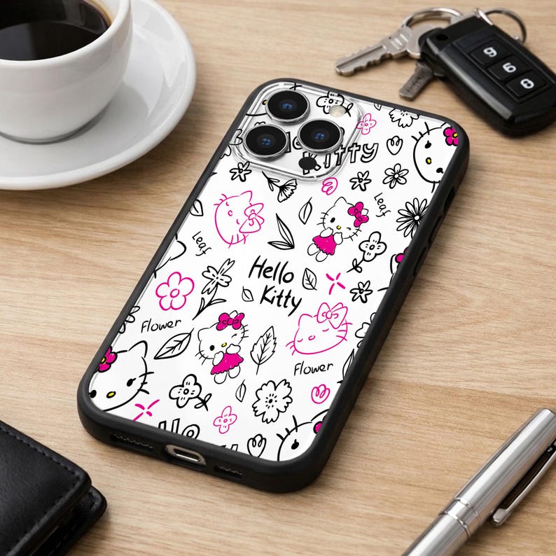 May include: A black phone case with a white background featuring a Hello Kitty design. The design includes pink Hello Kitty characters, flowers, and the text "Hello Kitty". The case is on a wooden surface.