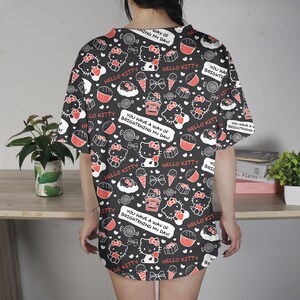 May include: Black, oversized t-shirt featuring a repeating pattern of Hello Kitty, cupcakes, ice cream cones, and bows. The shirt includes text that reads "Hello Kitty" and "You have a way of brightening my day!"