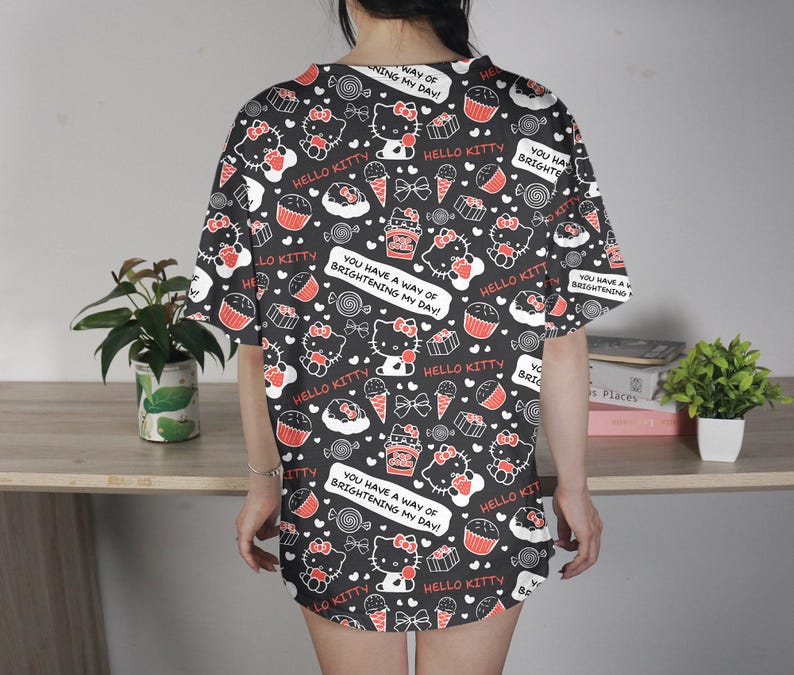 May include: Black, oversized t-shirt featuring a repeating pattern of Hello Kitty, cupcakes, ice cream cones, and bows. The shirt includes text that reads "Hello Kitty" and "You have a way of brightening my day!"