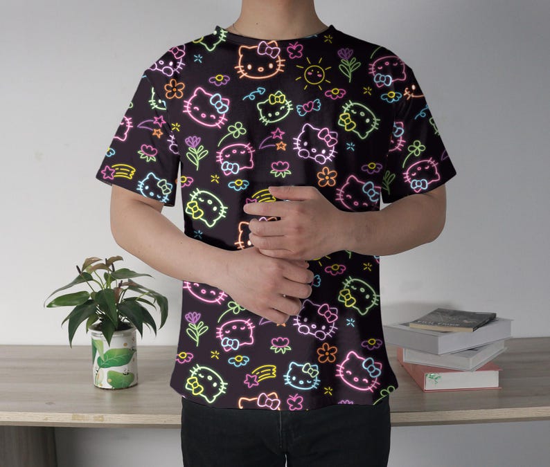May include: Black t-shirt featuring a neon-style pattern of Hello Kitty characters, flowers, stars, and rainbows. The design is in bright neon colors, creating a vibrant contrast against the dark background. The shirt has short sleeves and a crew neck.