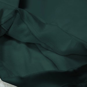 May include: Close-up of the inside of a dark green hooded sweatshirt. The fabric is soft and has a ribbed texture.