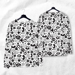 Peut inclure: Deux chemises &agrave; manches longues avec un motif Mickey Mouse noir et blanc. Le motif comprend des t&ecirc;tes de Mickey Mouse, des &eacute;toiles, des bulles et du texte comme "Mickey Mouse", "Oh Boy" et "Aw Shucks". Les chemises sont suspendues &agrave; des cintres noirs.