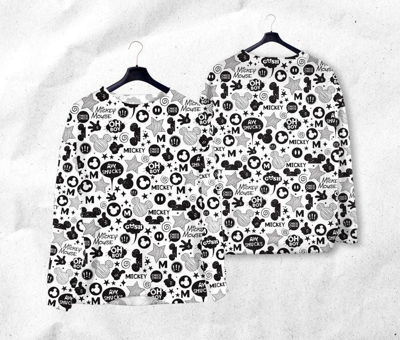 Peut inclure: Deux chemises &agrave; manches longues avec un motif Mickey Mouse noir et blanc. Le motif comprend des t&ecirc;tes de Mickey Mouse, des &eacute;toiles, des bulles et du texte comme "Mickey Mouse", "Oh Boy" et "Aw Shucks". Les chemises sont suspendues &agrave; des cintres noirs.
