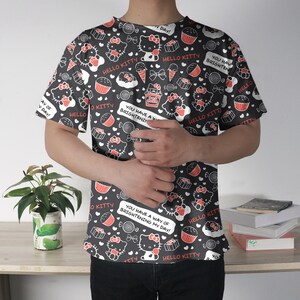 May include: Black t-shirt featuring a repeating pattern of Hello Kitty characters, cupcakes, ice cream cones, and candies. The design includes the text "Hello Kitty" and "You have a way of brightening my day!" in white. The shirt is short-sleeved.