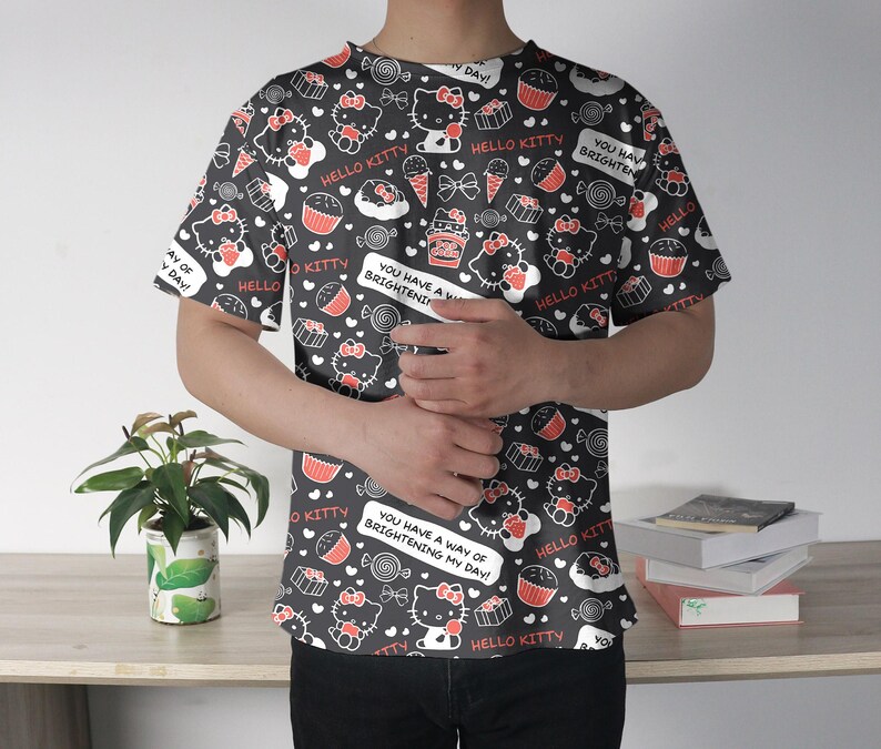 May include: Black t-shirt featuring a repeating pattern of Hello Kitty characters, cupcakes, ice cream cones, and candies. The design includes the text "Hello Kitty" and "You have a way of brightening my day!" in white. The shirt is short-sleeved.